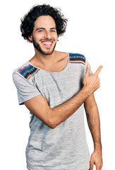 Young hispanic man wearing casual t shirt cheerful with a smile of face pointing with hand and finger up to the side with happy and natural expression on face