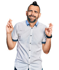 Hispanic man with ponytail wearing casual white shirt gesturing finger crossed smiling with hope and eyes closed. luck and superstitious concept.