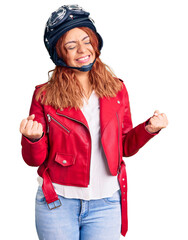 Young latin woman wearing leather jacket holding motorcycle helmet very happy and excited doing winner gesture with arms raised, smiling and screaming for success. celebration concept.