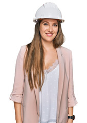 Young blonde woman wearing architect hardhat looking positive and happy standing and smiling with a confident smile showing teeth