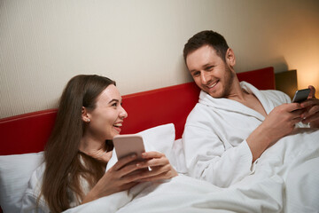 Happy couple with cellphones relaxing in hotel room