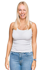 Fototapeta premium Young blonde girl wearing casual style with sleeveless shirt winking looking at the camera with sexy expression, cheerful and happy face.
