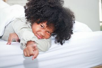 Little African American girl lying on bed with index finger forward. Young child development...