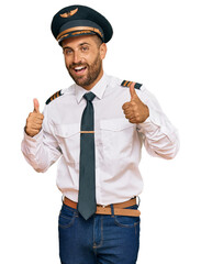 Handsome man with beard wearing airplane pilot uniform success sign doing positive gesture with hand, thumbs up smiling and happy. cheerful expression and winner gesture. © Krakenimages.com