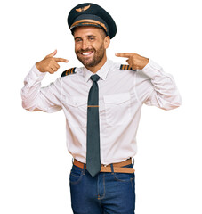 Handsome man with beard wearing airplane pilot uniform smiling cheerful showing and pointing with fingers teeth and mouth. dental health concept. © Krakenimages.com