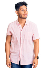 Handsome latin american young man wearing casual summer shirt looking away to side with smile on face, natural expression. laughing confident.