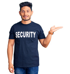 Handsome latin american young man wearing security t shirt smiling cheerful presenting and pointing with palm of hand looking at the camera.