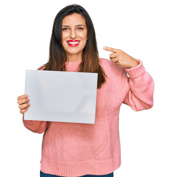 Beautiful hispanic woman holding blank empty banner pointing finger to one self smiling happy and proud