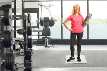 Full length portrait of a mature woman in sportswear holding an exercise mat at gym