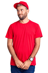 Young handsome blond man wearing t-shirt and cap smiling looking to the side and staring away thinking.