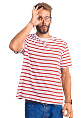 Handsome blond man with beard wearing casual clothes and glasses doing ok gesture shocked with surprised face, eye looking through fingers. unbelieving expression.
