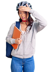 Young beautiful chinese girl wearing student backpack and bike helmet holding book stressed and frustrated with hand on head, surprised and angry face