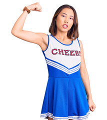 Young beautiful chinese girl wearing cheerleader uniform strong person showing arm muscle, confident and proud of power