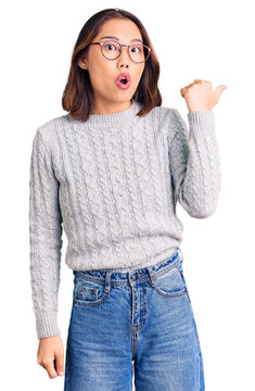 Young beautiful chinese girl wearing casual clothes surprised pointing with hand finger to the side, open mouth amazed expression.