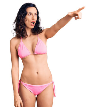 Young beautiful hispanic woman wearing bikini pointing with finger surprised ahead, open mouth amazed expression, something on the front