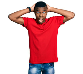 Fototapeta premium Young african american man wearing casual red t shirt crazy and scared with hands on head, afraid and surprised of shock with open mouth