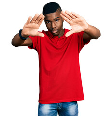 Fototapeta premium Young african american man wearing casual red t shirt doing frame using hands palms and fingers, camera perspective