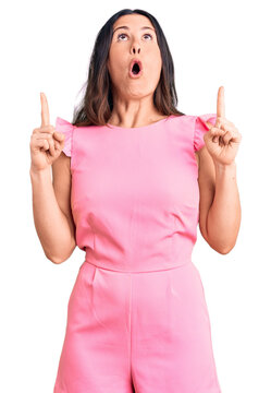 Young beautiful brunette woman wearing casual dress amazed and surprised looking up and pointing with fingers and raised arms.