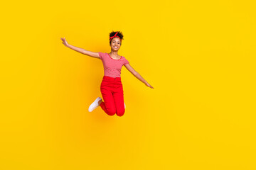 Full size photo of funky young girl jumping spread hands flight dressed stylish red striped clothes isolated on yellow color background