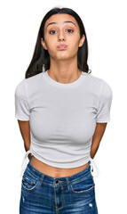 Young hispanic girl wearing casual white t shirt puffing cheeks with funny face. mouth inflated with air, crazy expression.