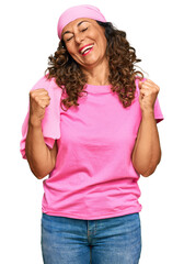 Fototapeta na wymiar Middle age hispanic woman wearing breast cancer support pink scarf very happy and excited doing winner gesture with arms raised, smiling and screaming for success. celebration concept.