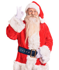 Old senior man with grey hair and long beard wearing traditional santa claus costume smiling positive doing ok sign with hand and fingers. successful expression.