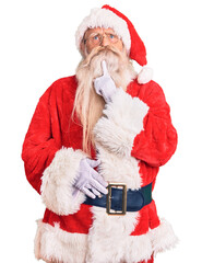 Old senior man with grey hair and long beard wearing traditional santa claus costume thinking...