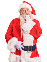 Old senior man with grey hair and long beard wearing traditional santa claus costume looking confident at the camera smiling with crossed arms and hand raised on chin. thinking positive.