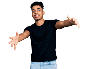 Young african american man wearing casual black t shirt looking at the camera smiling with open arms for hug. cheerful expression embracing happiness.