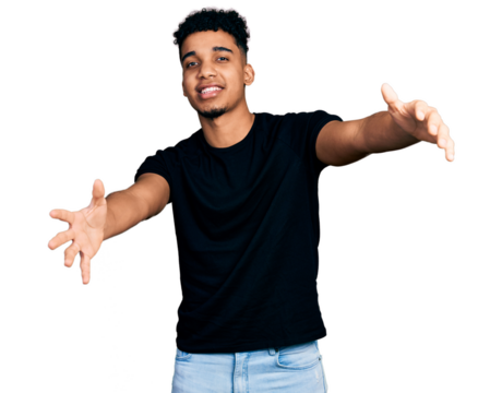 Young african american man wearing casual black t shirt looking at the camera smiling with open arms for hug. cheerful expression embracing happiness.