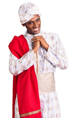 African handsome man wearing tradition sherwani saree clothes laughing nervous and excited with hands on chin looking to the side