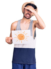 Young hispanic man wearing summer hat holding sun draw stressed and frustrated with hand on head,...