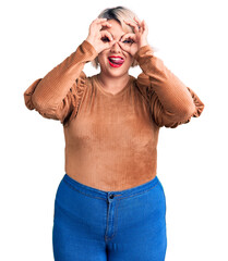 Fototapeta premium Young blonde plus size woman wearing casual sweater doing ok gesture like binoculars sticking tongue out, eyes looking through fingers. crazy expression.