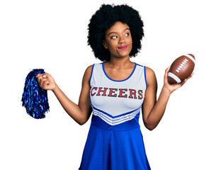 Young african american woman wearing cheerleader uniform holding pompom and football ball smiling...
