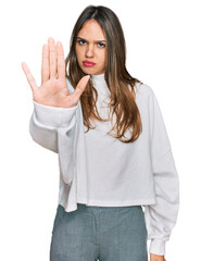 Young brunette woman wearing casual turtleneck sweater doing stop sing with palm of the hand. warning expression with negative and serious gesture on the face.