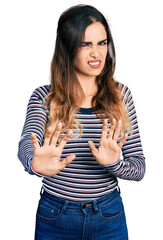 Beautiful hispanic woman wearing casual striped shirt disgusted expression, displeased and fearful doing disgust face because aversion reaction. with hands raised