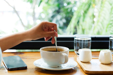 Asian woman's hand stirs the coffee spoon in the cup. so that the nectar poured into it is homogeneously dissolved Eating is more enjoyable than sitting in a coffee shop by the window.