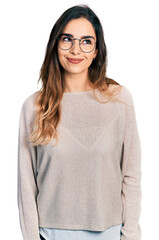 Beautiful hispanic woman wearing casual sweater and glasses smiling looking to the side and staring away thinking.
