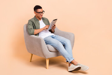 Full length photo of intelligent guy dressed khaki shirt glasses jeans look at tablet texting email...