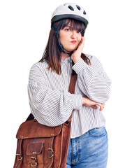 Young plus size woman wearing bike helmet and leather bag thinking looking tired and bored with depression problems with crossed arms.