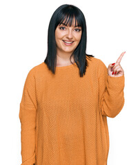 Young hispanic woman wearing casual clothes with a big smile on face, pointing with hand finger to the side looking at the camera.