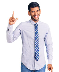 Young latin man wearing business clothes pointing finger up with successful idea. exited and happy. number one.