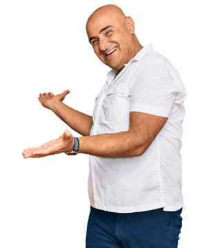 Mature middle east man with mustache wearing casual white shirt inviting to enter smiling natural with open hand