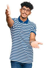 Naklejka premium Young arab man wearing casual clothes and glasses looking at the camera smiling with open arms for hug. cheerful expression embracing happiness.