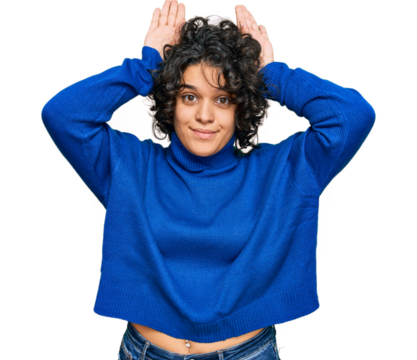 Young hispanic woman with curly hair wearing turtleneck sweater doing bunny ears gesture with hands palms looking cynical and skeptical. easter rabbit concept.