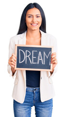 Young beautiful latin girl holding blackboard with dream word looking positive and happy standing and smiling with a confident smile showing teeth