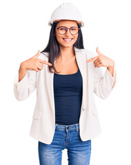 Obraz na płótnie Canvas Young beautiful latin girl wearing architect hardhat and glasses looking confident with smile on face, pointing oneself with fingers proud and happy.
