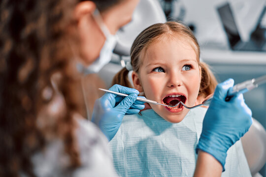 Children's dentistry. First examination at the dentist. A cute beautiful girl with an open mouth is looking to the side while the doctor is treating her teeth.