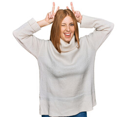 Young irish woman wearing casual winter sweater posing funny and crazy with fingers on head as...