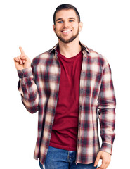Naklejka premium Young handsome man wearing casual shirt with a big smile on face, pointing with hand finger to the side looking at the camera.